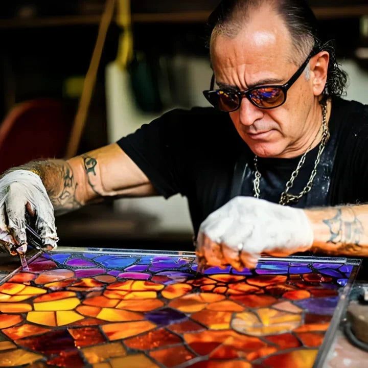 Handwerker mit Sonnenbrille setzt bunte Glasstücke für ein Mosaik aus orangefarbenem und violettem Glas zusammen 2