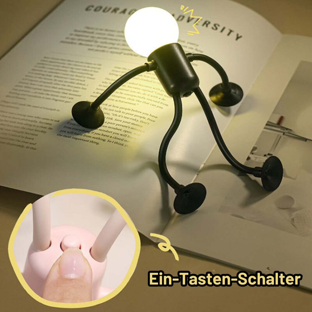 Schwarzes Männchen-Licht mit Saugnäpfen steht auf einem aufgeschlagenen Buch und beleuchtet die Seiten; Ausschnitt zeigt den Schalter am Rumpf. 10
