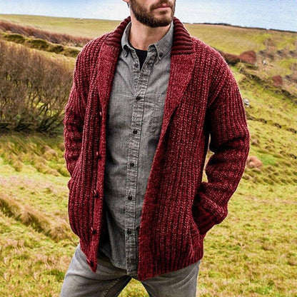 Mann in roter Strickjacke und grauem Hemd in ländlicher Landschaft.