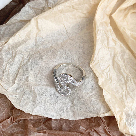 Silberner, verstellbarer Ring mit geschwungenem Design auf braunem Papierhintergrund.