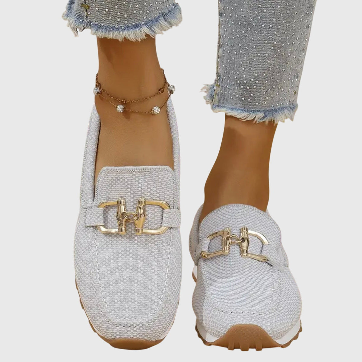 Frontansicht hellgrauer Slipper mit goldener Zierspange, getragen mit Fußkettchen und Jeans mit Strassbesatz 2