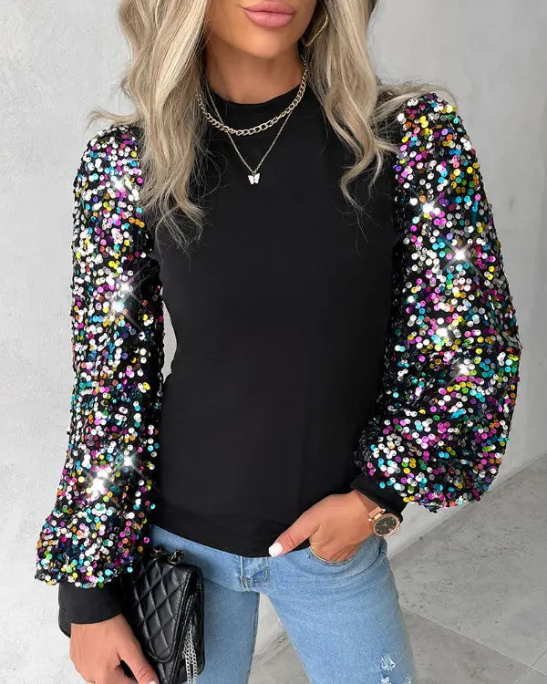 Frau in schwarzem Pullover mit bunten Paillettenärmeln, blaue Jeans, schwarze Tasche.