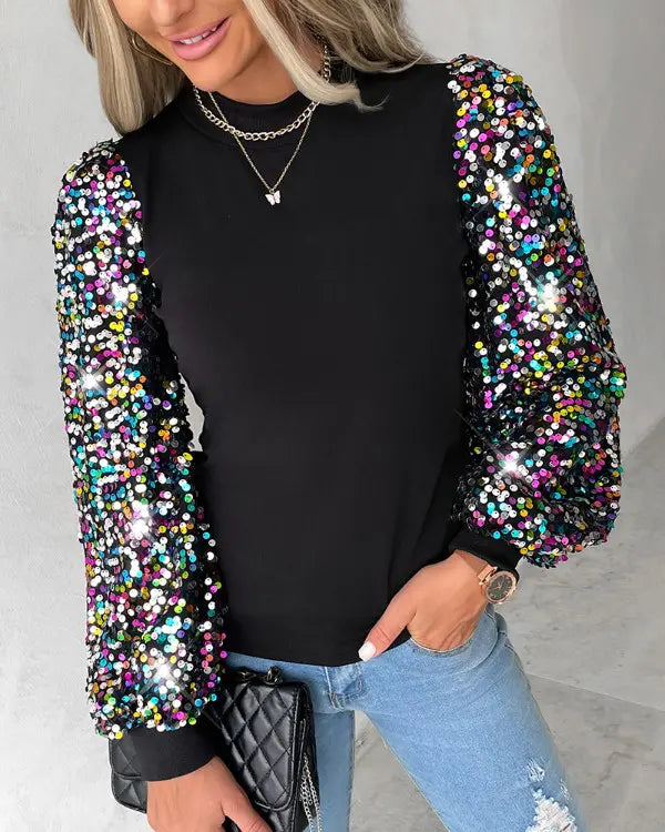 Frau in schwarzem Pullover mit bunten Paillettenärmeln, blaue Jeans, schwarze Tasche.