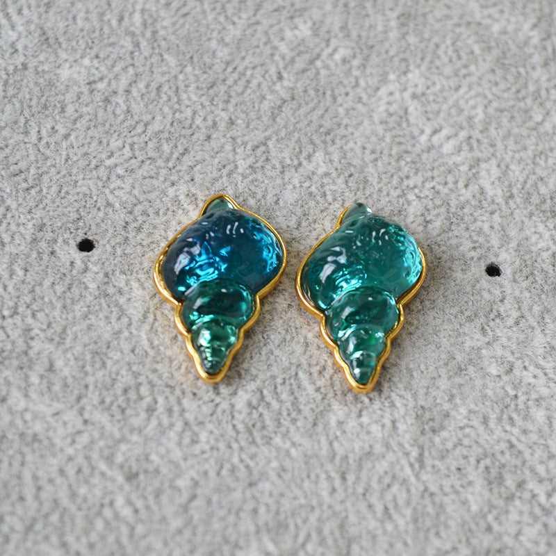 Blaue und grüne Muschel-Ohrringe, goldumrandet, auf grauem Hintergrund, Modeschmuck.