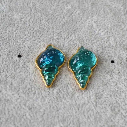 Blaue und grüne Muschel-Ohrringe, goldumrandet, auf grauem Hintergrund, Modeschmuck.