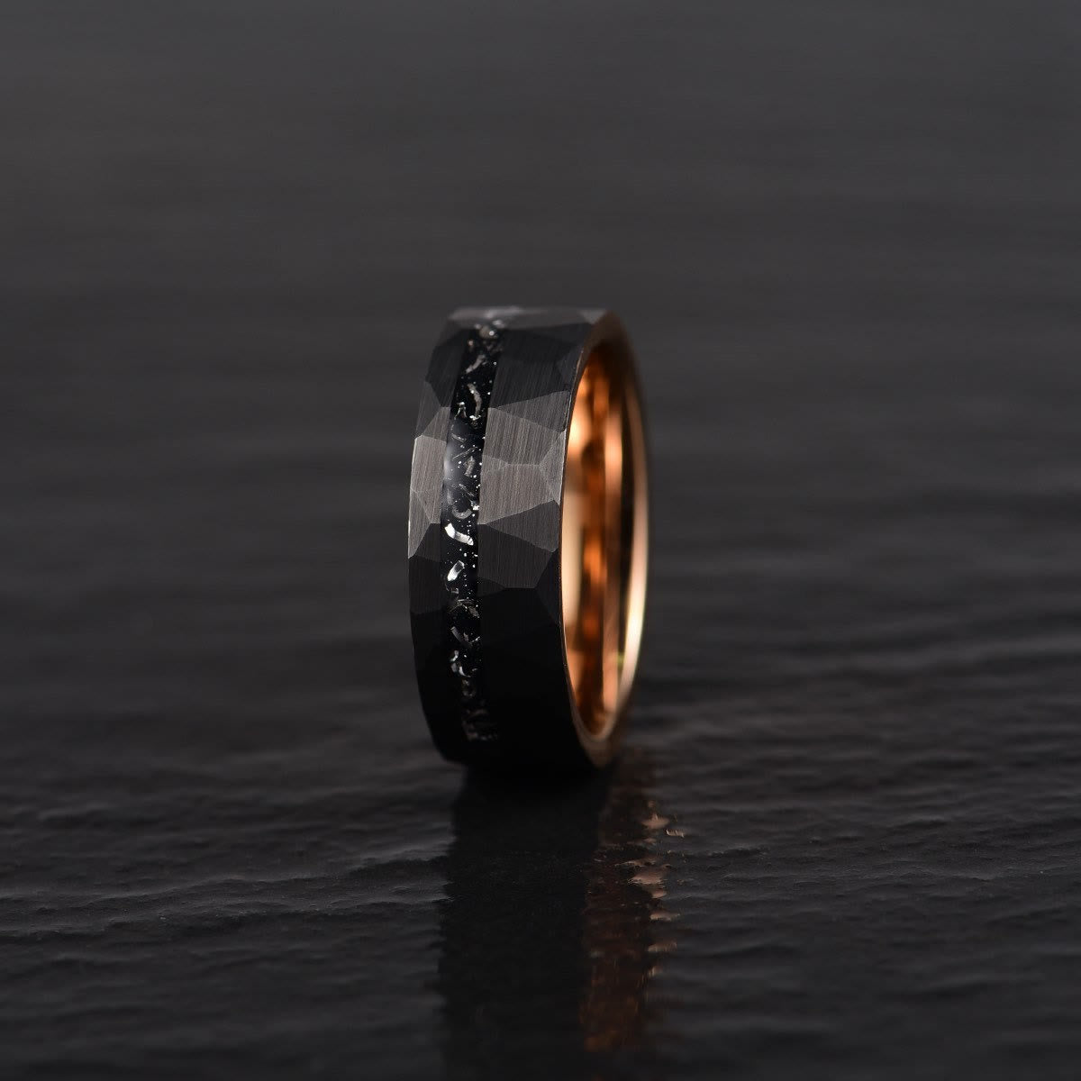 Schwarzer Wolframring mit facettierter Oberfläche und goldener Innenseite auf dunklem Hintergrund.