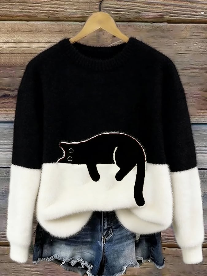 Schwarz-weißer Flauschpullover mit schwarzer Katze auf Kleiderbügel vor Holzwand, darunter Jeansshorts 6