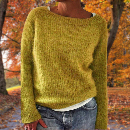 Senfgelber Strickpullover mit Rundhalsausschnitt, getragen über einem weißen Shirt und Jeans vor herbstlichem Laubwald. 1