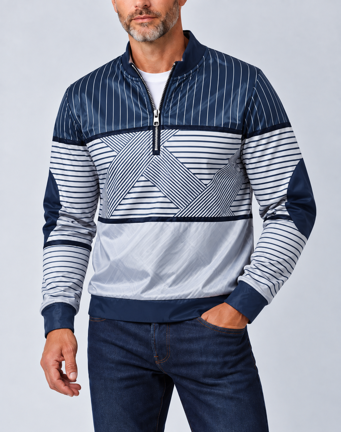 Mann mit grauem Bart trägt den marineblau-weiß gestreiften Pullover mit halbem Reißverschluss zu dunkler Jeans, eine Hand in der Hosentasche. 1