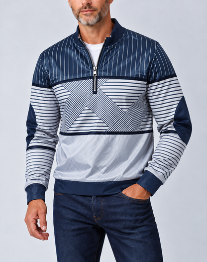 Mann mit grauem Bart trägt den marineblau-weiß gestreiften Pullover mit halbem Reißverschluss zu dunkler Jeans, eine Hand in der Hosentasche. 1