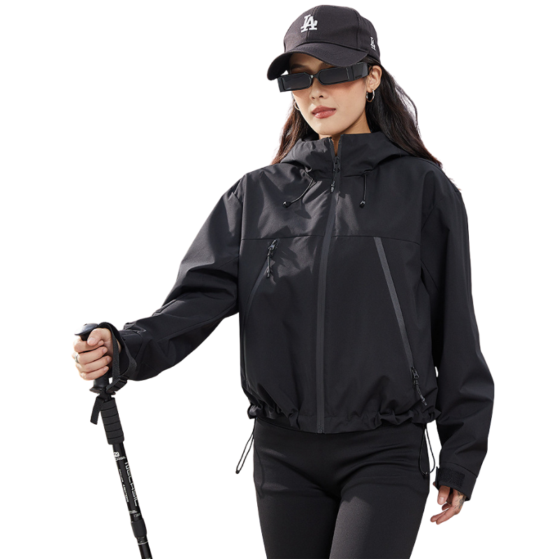 Schwarze Kapuzenjacke mit verstellbarem Saum an einer Frau mit schwarzer Kappe, die einen Trekkingstock hält 14