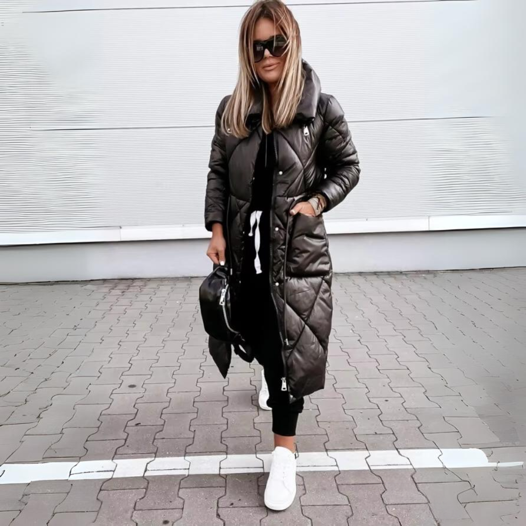 Frau mit Sonnenbrille trägt den langen schwarzen Steppmantel geschlossen, eine Hand in der aufgesetzten Tasche, dazu weiße Sneaker. 5
