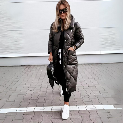 Frau mit Sonnenbrille trägt den langen schwarzen Steppmantel geschlossen, eine Hand in der aufgesetzten Tasche, dazu weiße Sneaker. 5