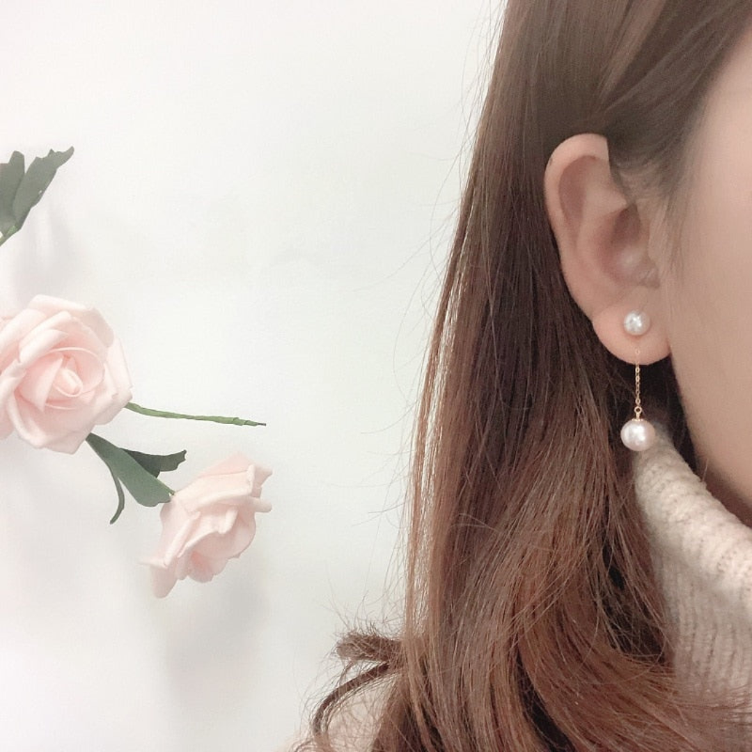 Frau mit Perlenohrringen, rosa Rosen im Hintergrund, eleganter Schmuck, Nahaufnahme.