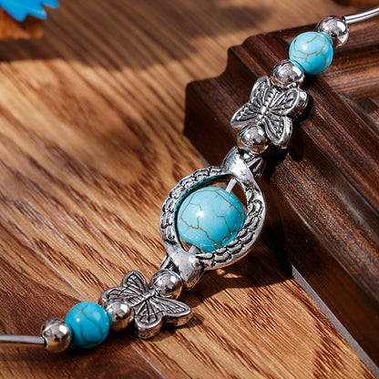 Silbernes Armband mit türkisfarbenen Steinen und Schmetterlingsdesign auf Holzoberfläche.