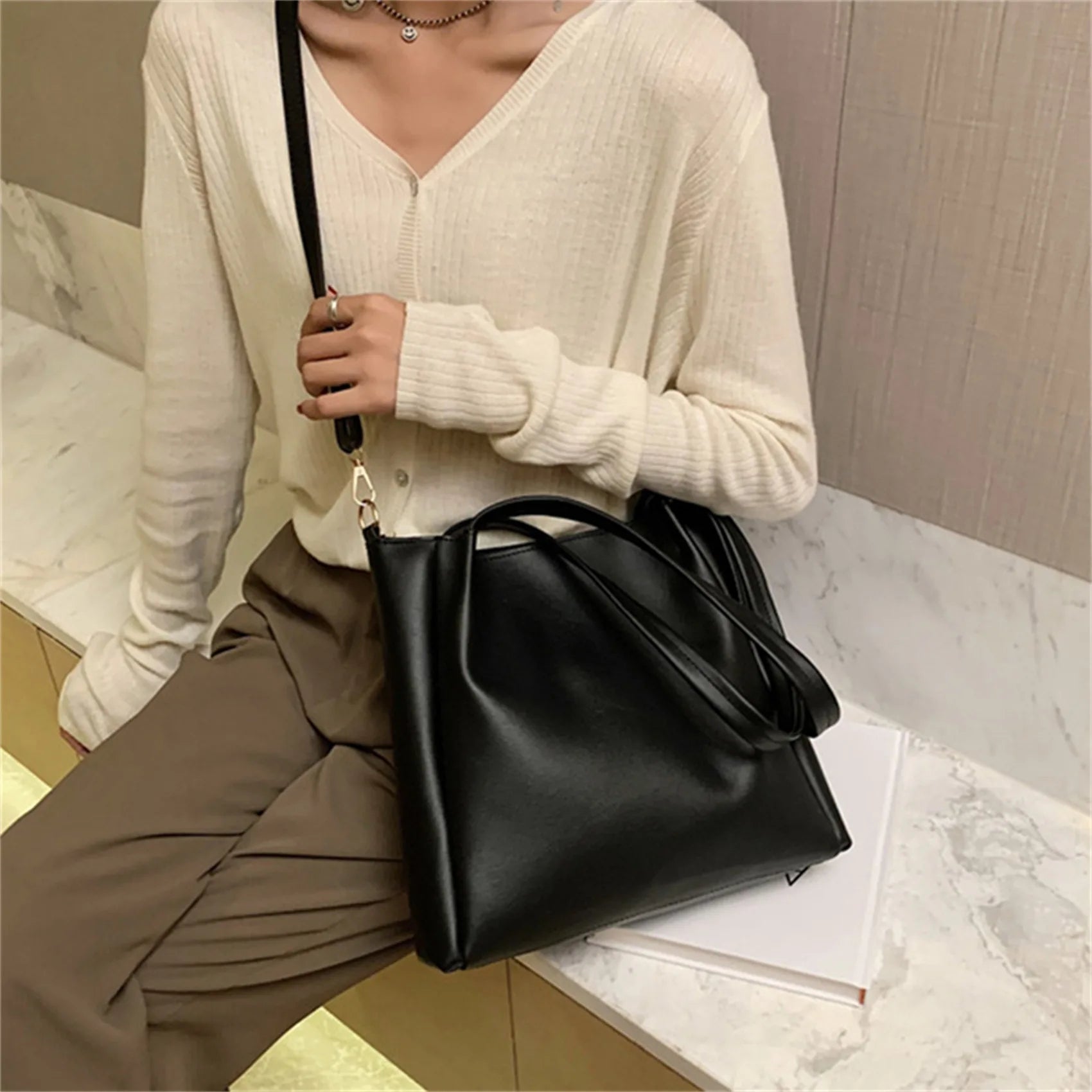 Frau mit schwarzer Lederhandtasche, lässiger Stil, beige Strickjacke, braune Hose.