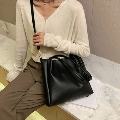 Frau mit schwarzer Lederhandtasche, lässiger Stil, beige Strickjacke, braune Hose.