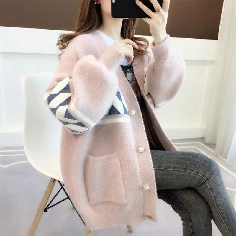 Frau trägt rosa Strickjacke mit geometrischem Muster, sitzt auf weißem Stuhl, modisch, gemütlich.