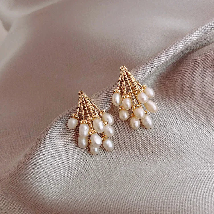 Goldene Ohrringe mit weißen Perlen auf beigem Satin, eleganter Schmuck für Damen.
