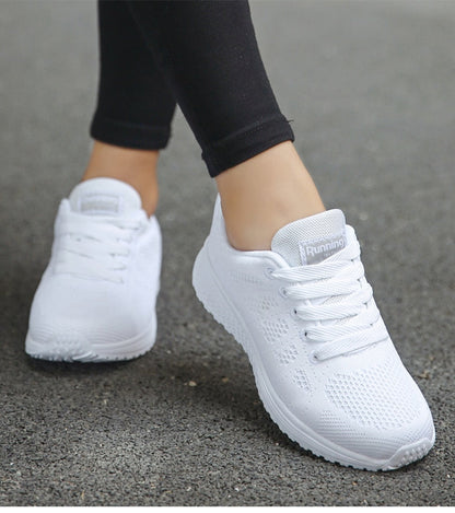 Weiße Damen-Laufschuhe, atmungsaktiv, mit Schnürsenkeln, auf Asphalt getragen.