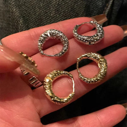 Vier runde, glitzernde Ohrringe in Silber und Gold auf einer Hand, modischer Schmuck.