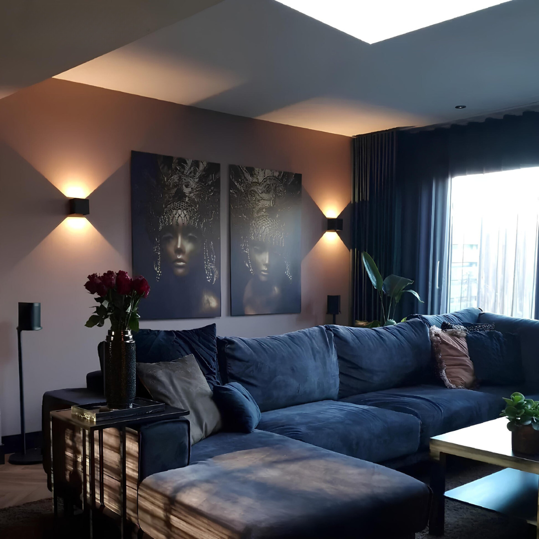 Zwei schwarze Würfelleuchten beleuchten die Wand im Wohnzimmer mit blauem Sofa, zwei Porträtbildern und dunklen Vorhängen. 9