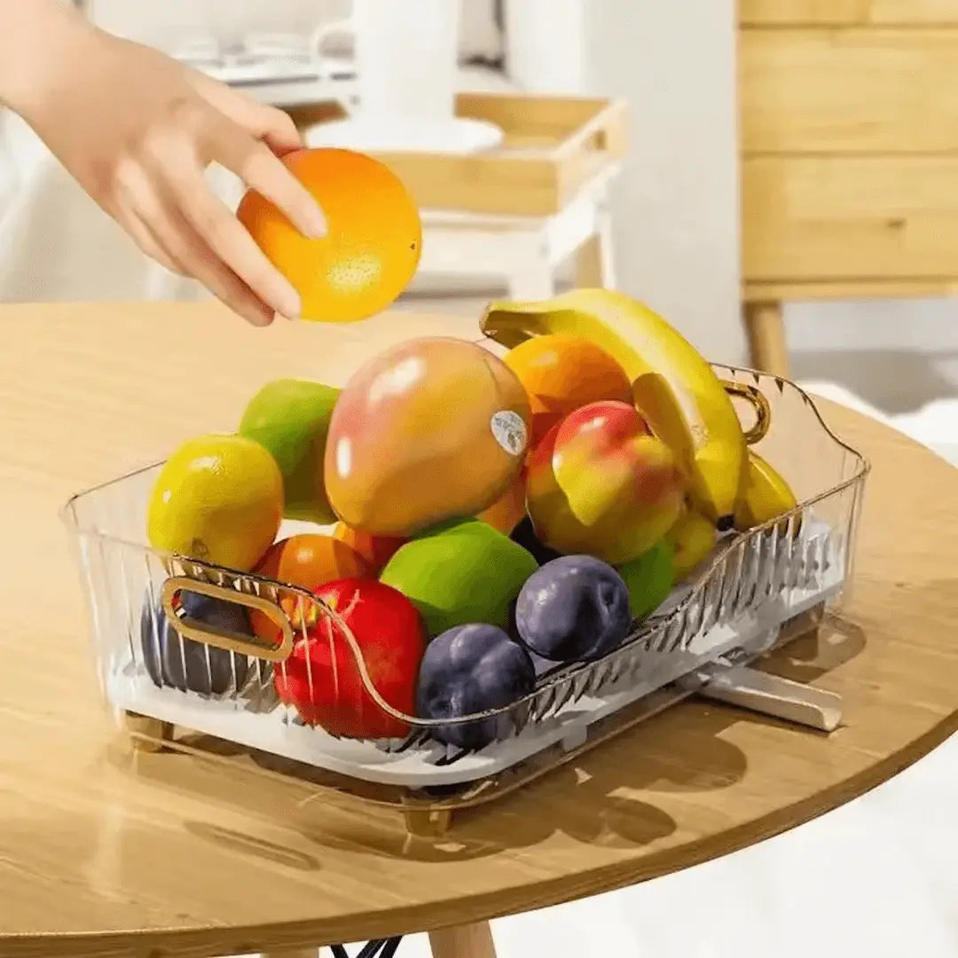 Hand greift nach Orange in Obstschale mit Bananen, Äpfeln, Pflaumen auf Holztisch.