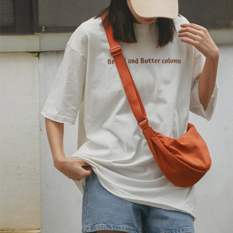 Frau mit weißem T-Shirt, roter Umhängetasche, Jeansshorts, beige Kappe, lässiger Stil.