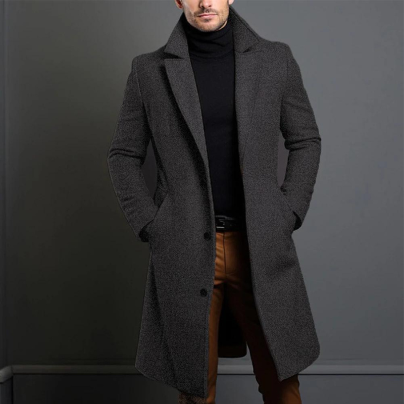 Der lange Mantel in meliertem Dunkelgrau mit leicht rauer Wollstruktur, getragen zu schwarzem Rollkragenpullover und brauner Hose. 3