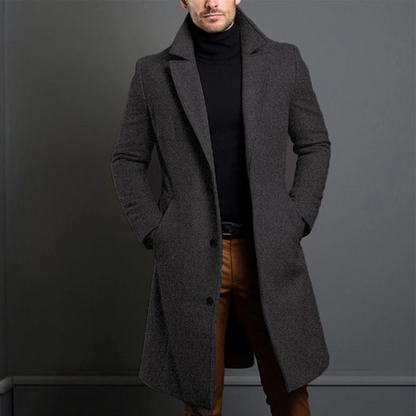 Der lange Mantel in meliertem Dunkelgrau mit leicht rauer Wollstruktur, getragen zu schwarzem Rollkragenpullover und brauner Hose. 3