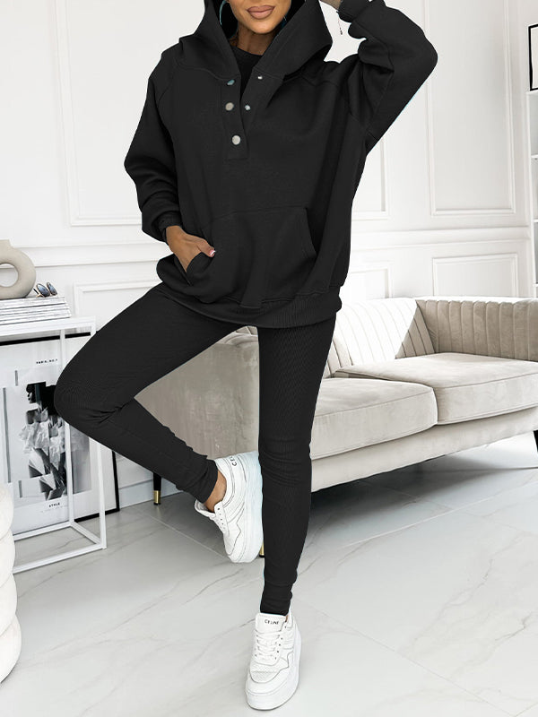 Frau in schwarzem Hoodie und Leggings, weiße Sneakers, modernes Wohnzimmer, Freizeitmode.