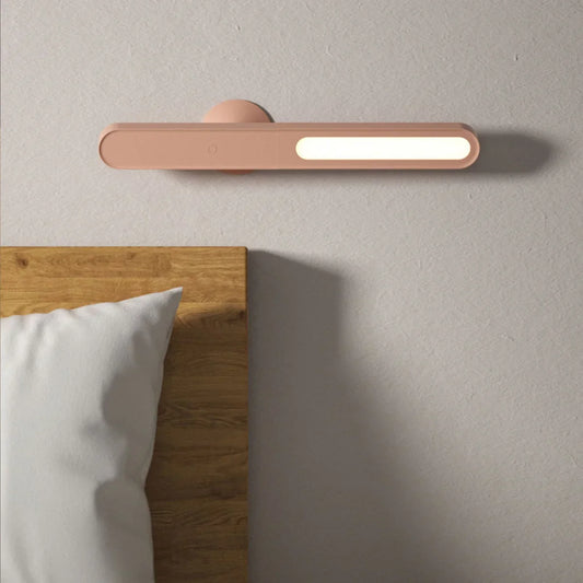 Moderne LED-Wandleuchte in Rosa über Holz-Bettkopfteil, minimalistisch, energiesparend.
