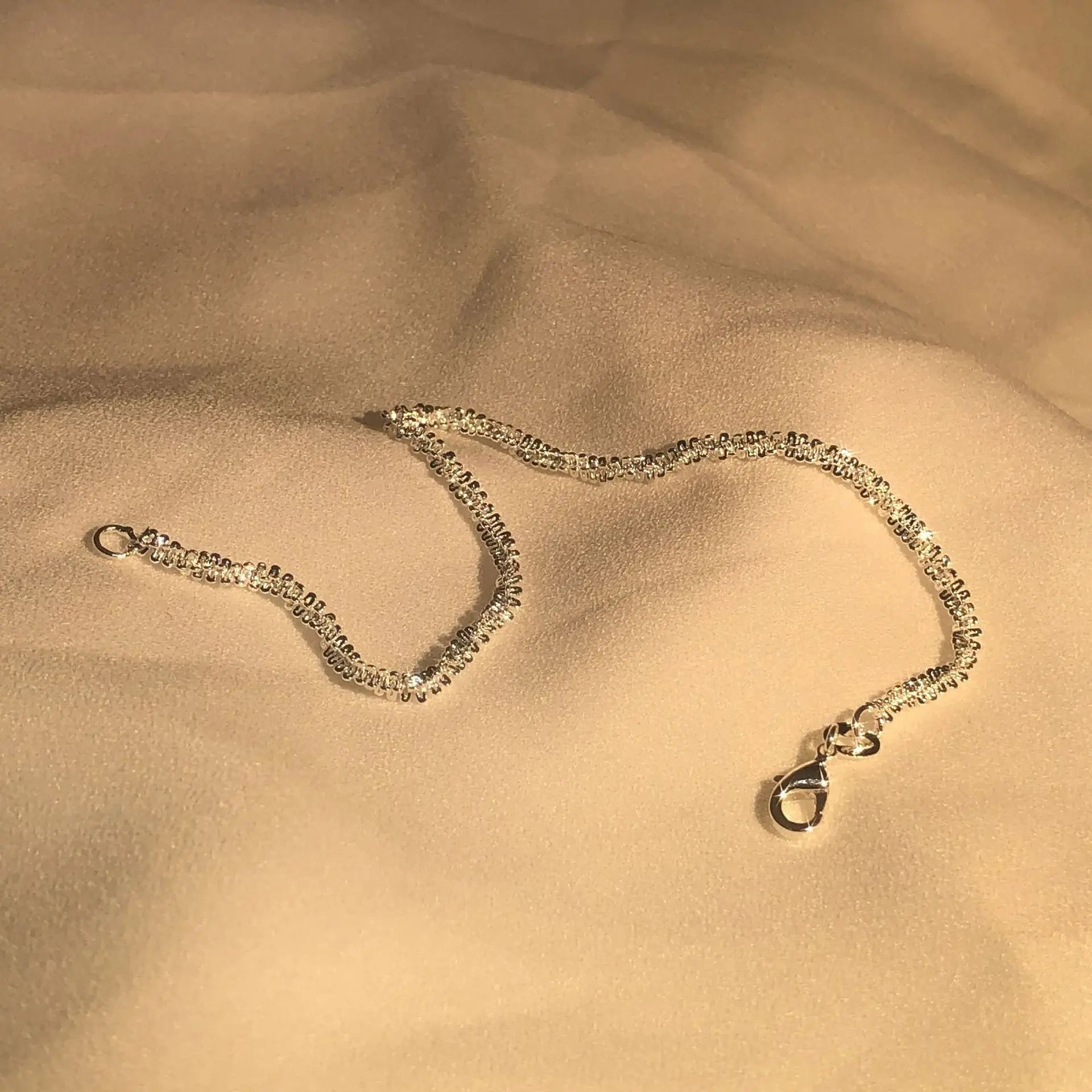 Silberne Halskette auf beigem Stoff, elegantes Schmuckdesign, Damenaccessoire.