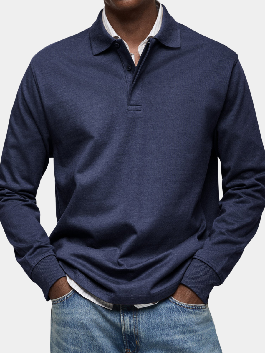 Nahaufnahme des Langarm-Poloshirts in Marineblau, getragen von einem Model mit Händen in den Jeanstaschen über gestreiftem Hemd. 1