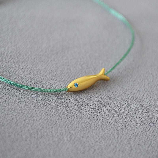 Goldener Fischanhänger auf grünem Armband, minimalistisches Schmuckdesign, Geschenkidee.