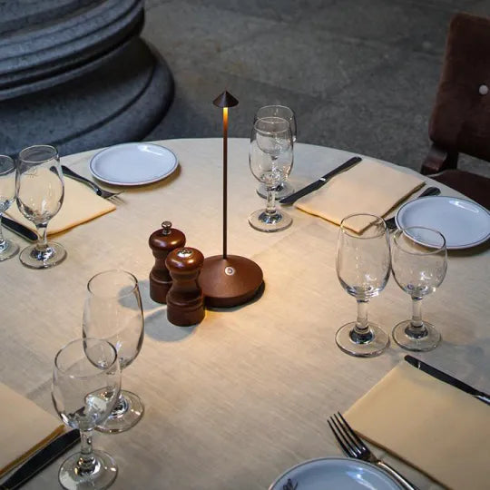 Runder Esstisch mit Tischlampe, Weingläsern, Tellern und Salz-Pfeffer-Streuer, elegantes Ambiente.