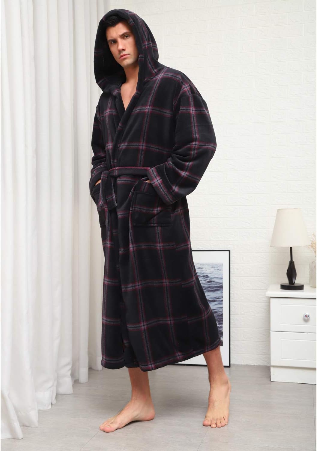 Mann im karierten, schwarzen Fleece-Bademantel mit Kapuze, stehend im Schlafzimmer.
