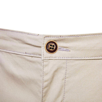 Nahaufnahme des braunen Knopfs mit Knopfloch am Bund der beigen Shorts, umgeben von hellen Steppnähten. 5