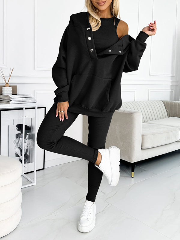 Frau in schwarzem Oversize-Sweatshirt und Leggings, weiße Sneaker, modernes Wohnzimmer.
