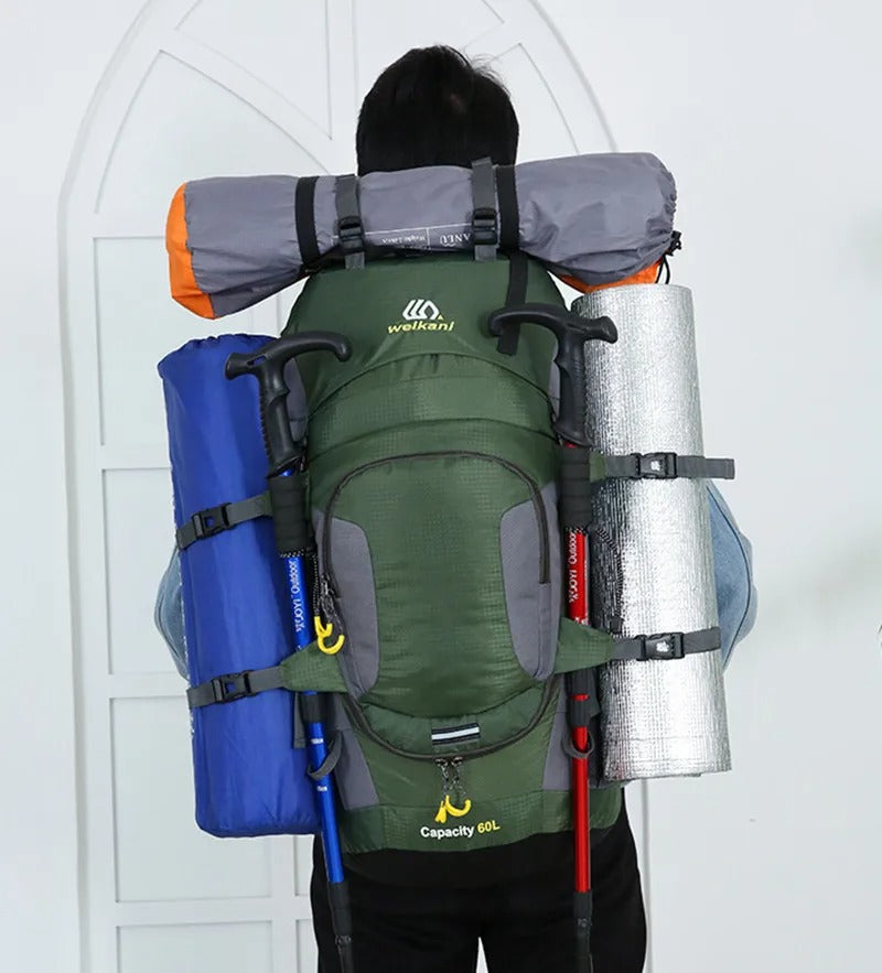 Mann mit grünem 60L Wanderrucksack, Isomatte, Zelt, Trekkingstöcke, Outdoor-Ausrüstung.