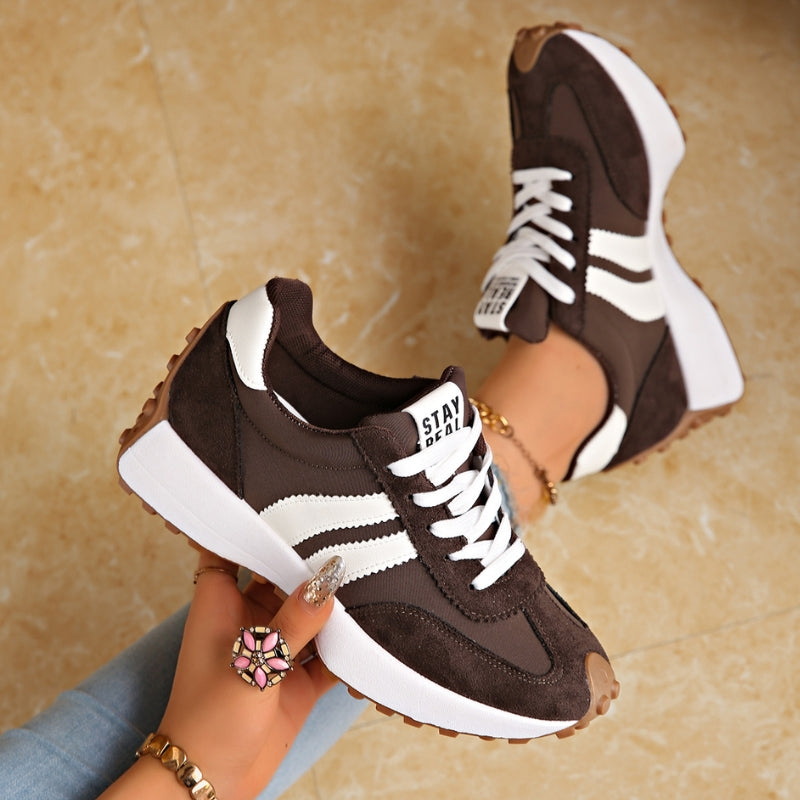 Dunkelbraune Sneaker mit weißen Streifen, ein Schuh in der Hand gehalten, der andere am Fuß 3