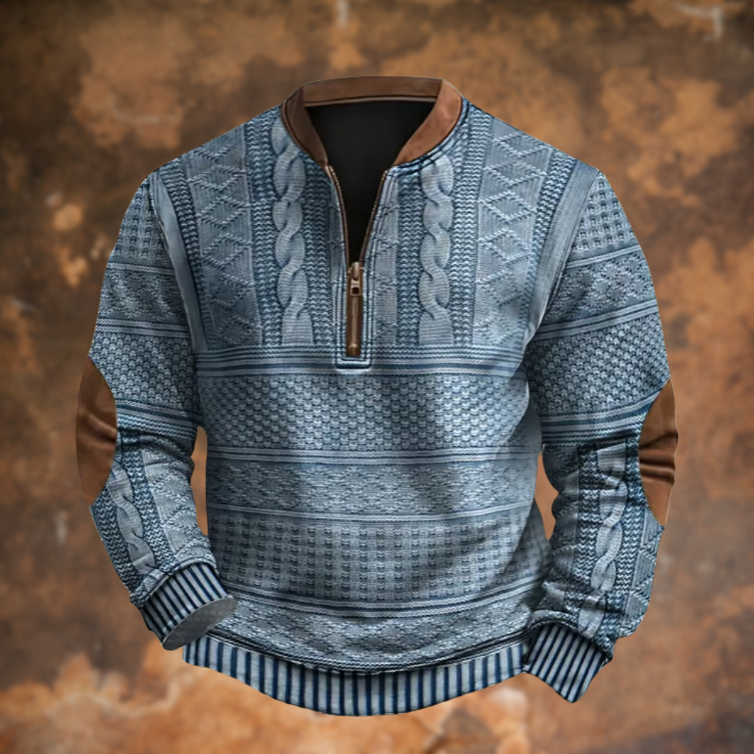 Frontansicht des Pullovers in Blaugrau mit Zopfmuster, Stehkragen, Halbreißverschluss, braunen Ellbogenflicken und gestreiften Bündchen vor rostbraunem Hintergr 1