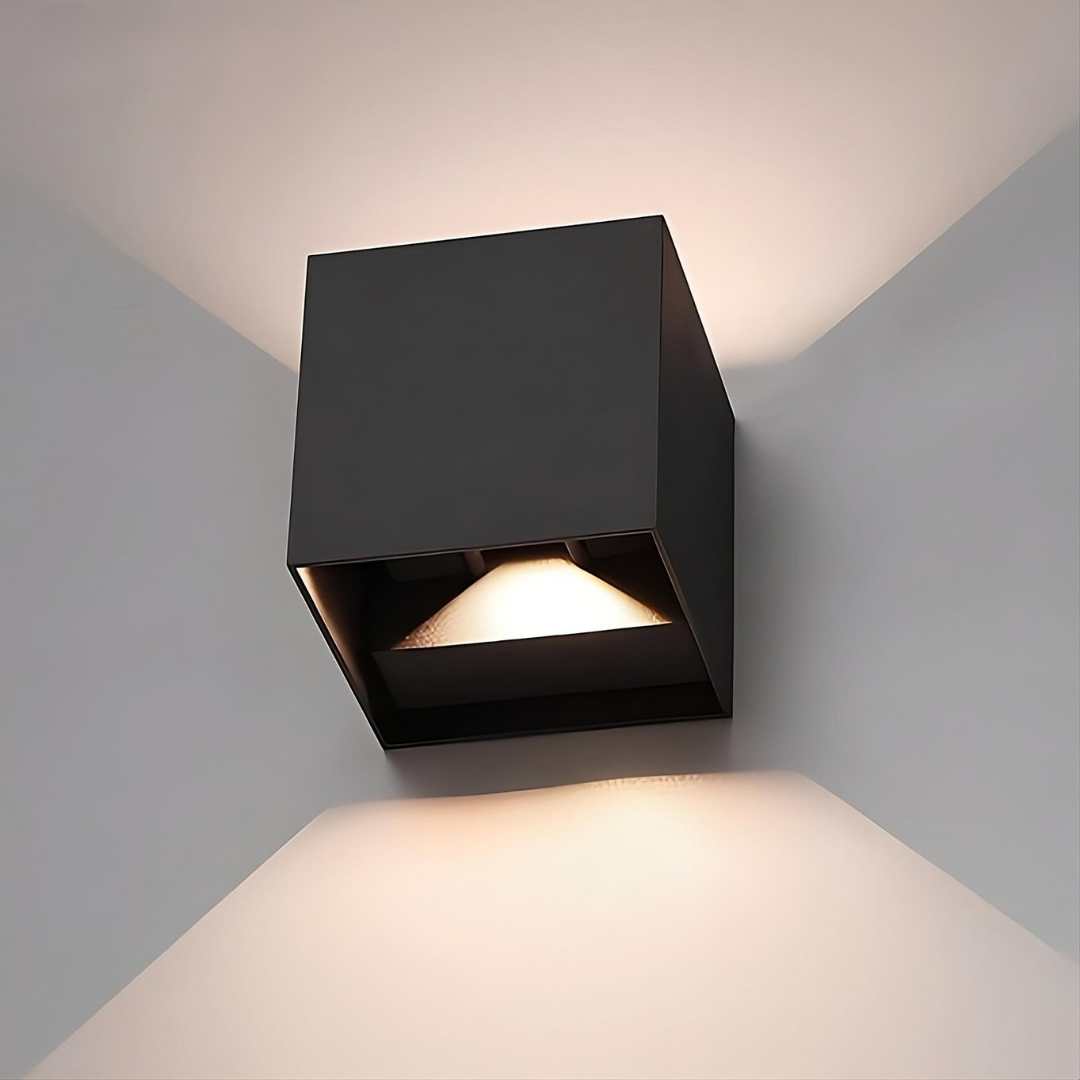 Nahaufnahme einer schwarzen Würfelleuchte mit sichtbarer Öffnung und LED-Modul, die Licht an die Wand wirft. 16