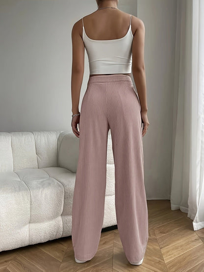 Frau in weißem Top und rosa Plisseehose, stehend vor einem weißen Sofa im modernen Wohnzimmer.