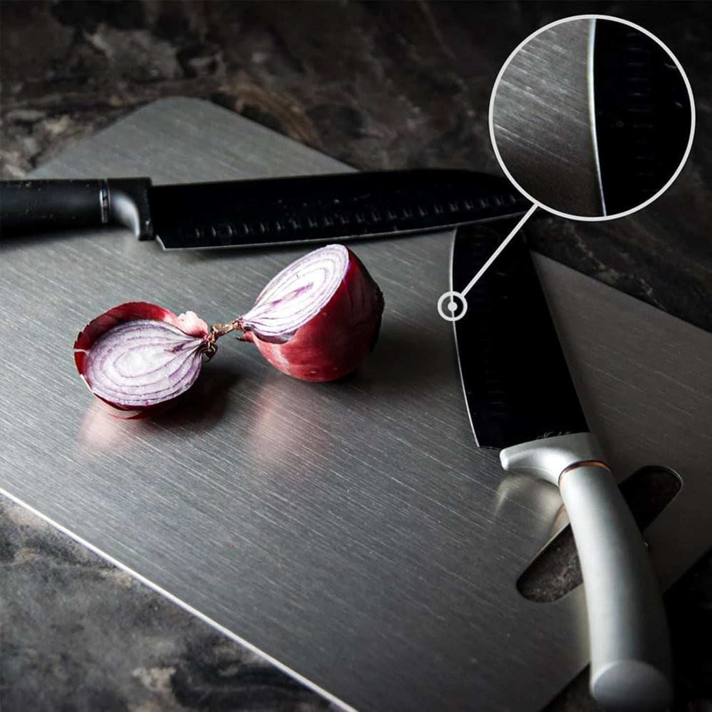 Zwei Küchenmesser auf Edelstahl-Schneidebrett mit halbierter roter Zwiebel, Nahaufnahme der Klinge.