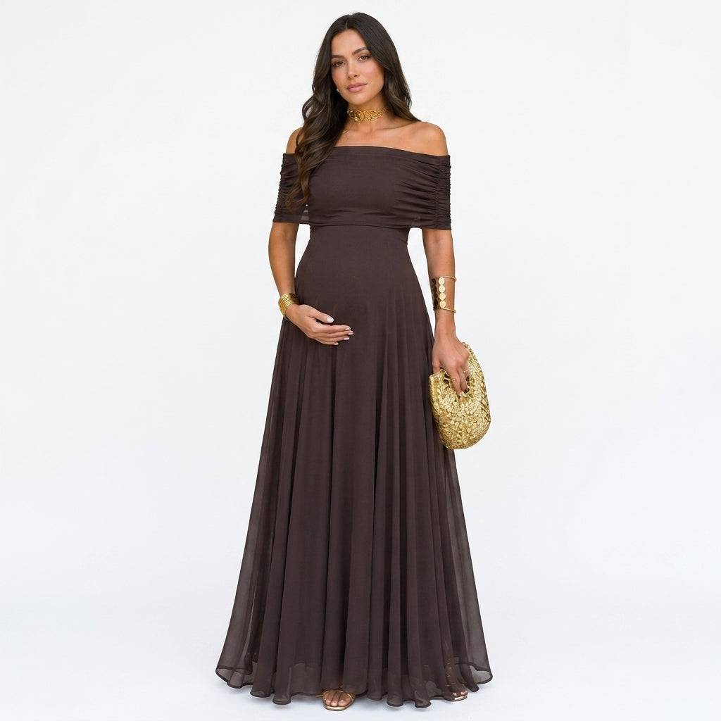 Schwangere Frau im dunkelbraunen, schulterfreien Chiffon-Maxikleid, frontal vor weißem Hintergrund, mit goldener Clutch und 1