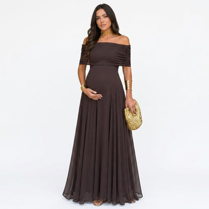 Schwangere Frau im dunkelbraunen, schulterfreien Chiffon-Maxikleid, frontal vor weißem Hintergrund, mit goldener Clutch und 1