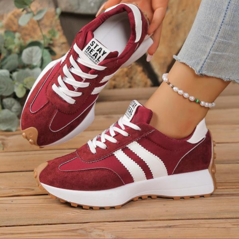 Weinrote Sneaker mit weißen Streifen, getragen auf Holzboden, daneben Pflanzen und eine Perlenkette am Knöchel 4