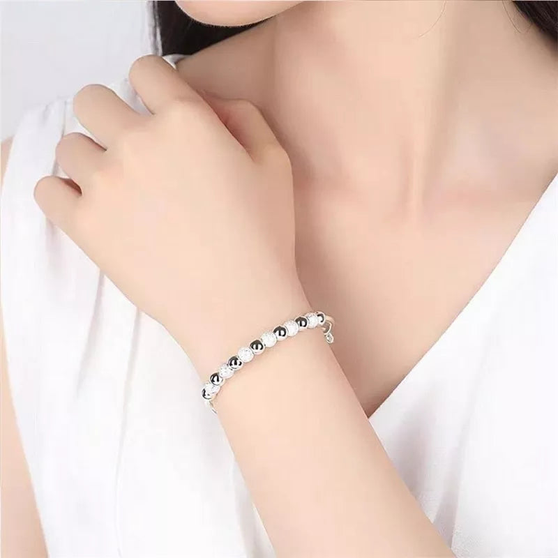 Frau trägt elegantes Silberarmband mit Perlen auf weißem Hintergrund.