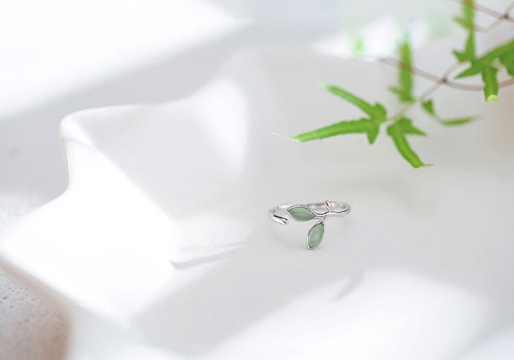 Silberner Ring mit grünen Blättern, verstellbar, auf weißem Keramikteller, Schmuckdesign.